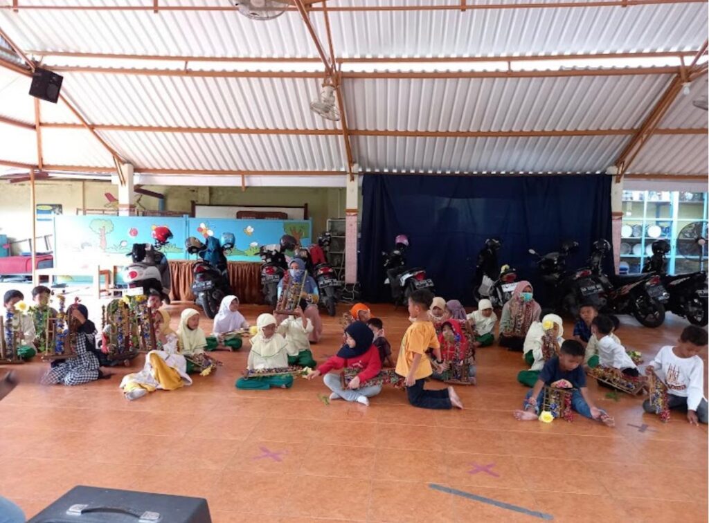 Group of children in a shaded hall sit on the floor displaying tall colorful trophy towers